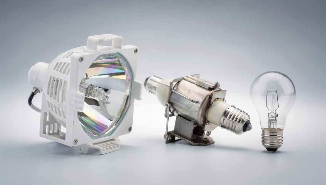 A projector lamp module and bare burner photographed beside an ordinary household light bulb for scale and contrast